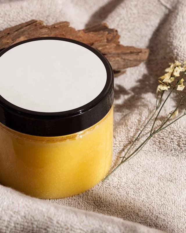Composição ilustrativa de pote de creme, tecido, madeira e flores secas.